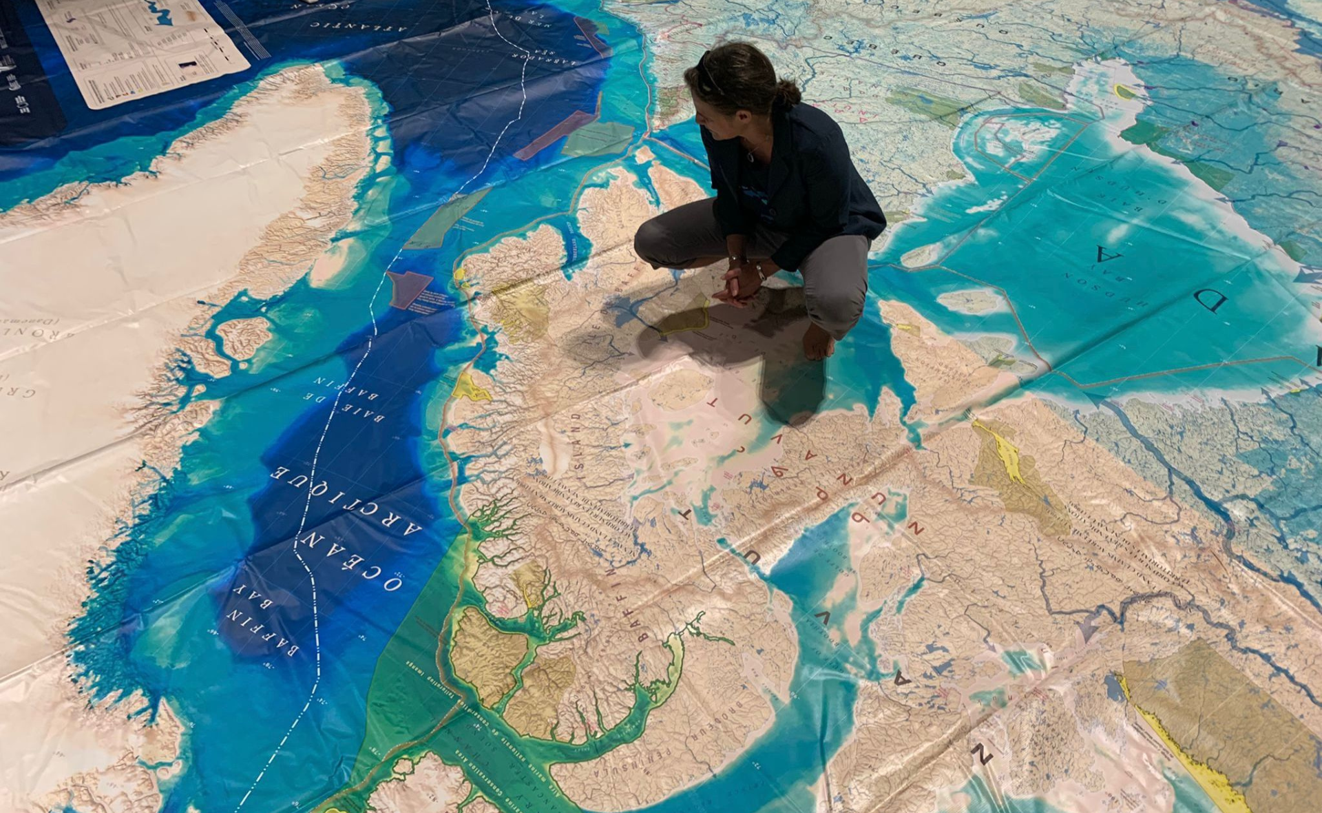 Une femme s'agenouille sur une carte géante créée par CanGEO pour être utilisée avec la carte de réalité augmentée de la Semaine de l'océan au Canada. La carte montre les eaux du Canada.