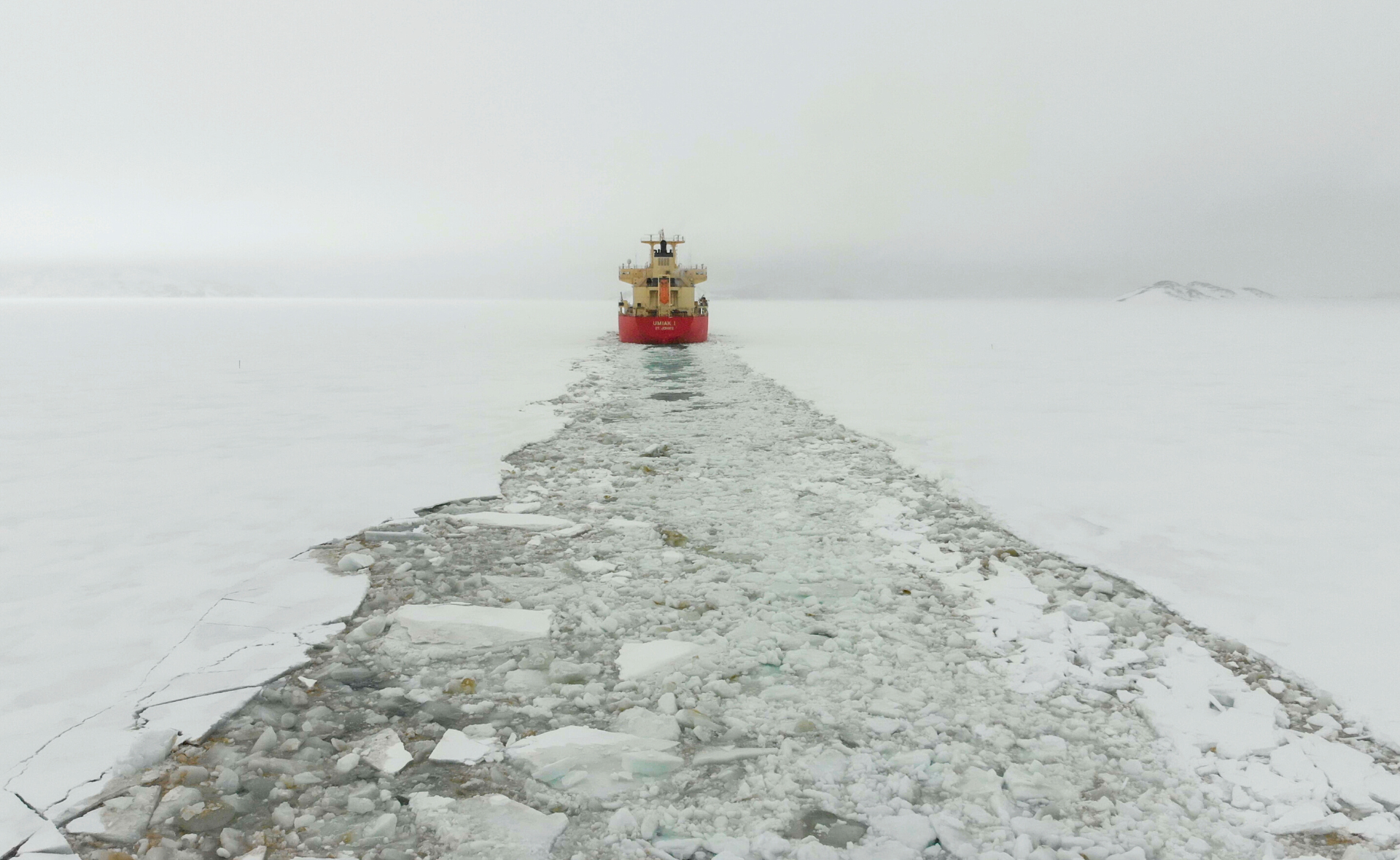 Un bateau traverse une grande surface d'eau glacée et laisse un sillon de morceaux de glace derrière lui.