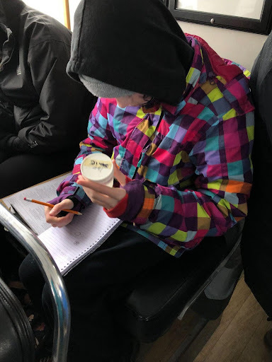 Un élève portant une veste colorée écrit dans un carnet tout en tenant un échantillon dans l'autre main.