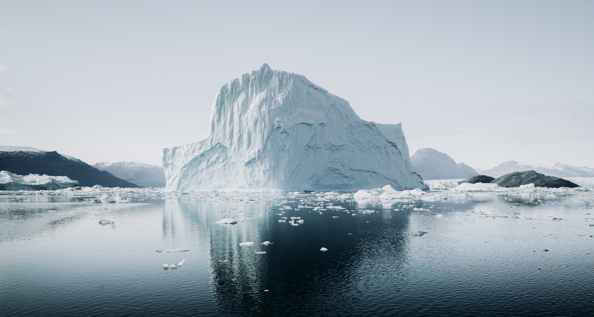 Iceberg in the middle of a water body in Greenland. In the background, a mountain range.