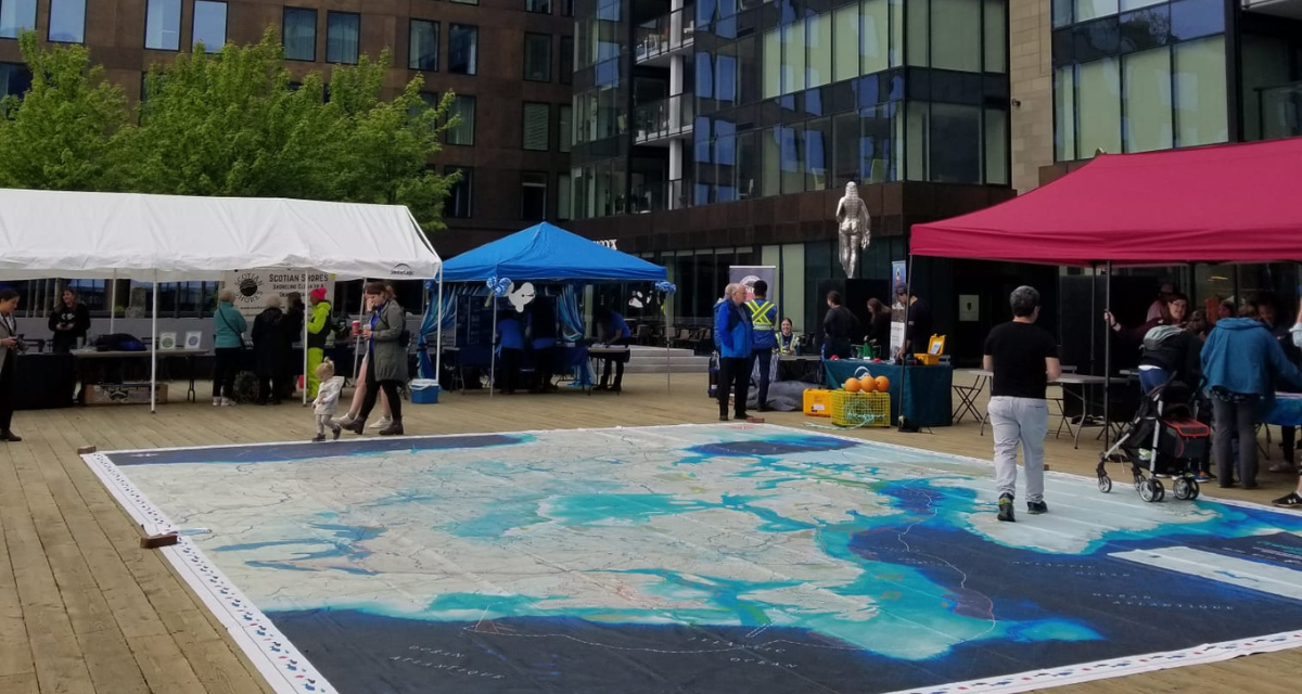 The Ocean, Freshwater and Us giant floor map is spread out on the floor. Around it are booths of different ocean organizations.