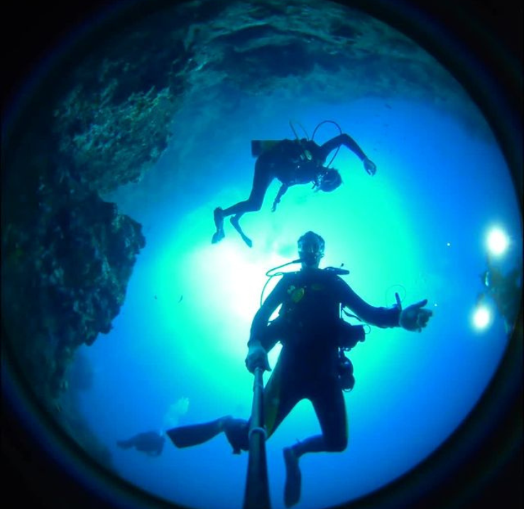 A view from a 360-degree camera showing two scuba divers floating in blue water.