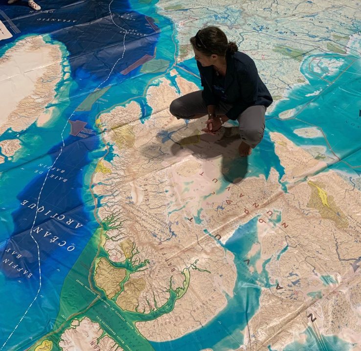 Une femme s'agenouille sur une carte géante créée par CanGEO pour être utilisée avec la carte de réalité augmentée de la Semaine de l'océan au Canada. La carte montre les eaux du Canada.