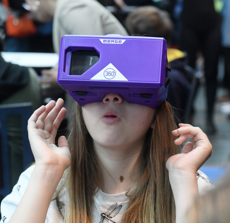 Une jeune fille aux cheveux longs est étonnée par ce qu'elle voit dans son casque de réalité virtuelle violet.