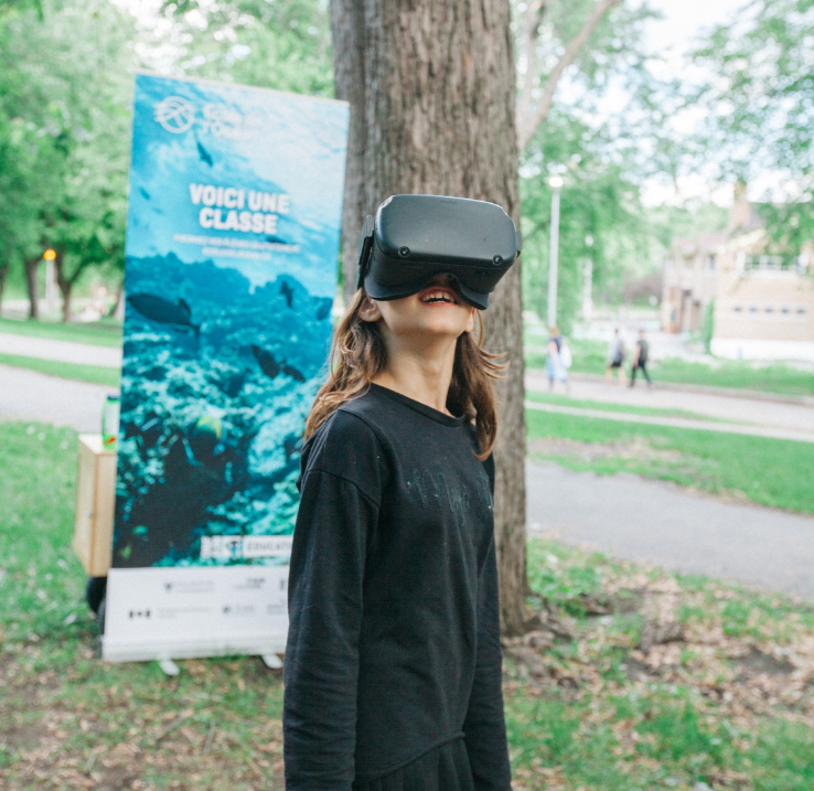 Outside, a child tries out Ocean School resources with a VR headset. In the background is an Ocean School promotional banner.
