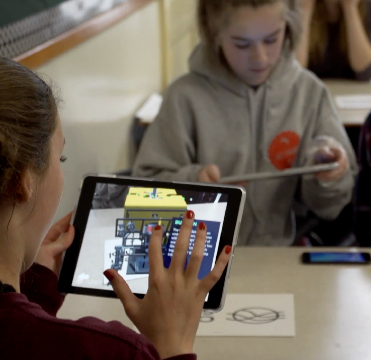 Students looking at an augmented reality model of a robot on tablets.