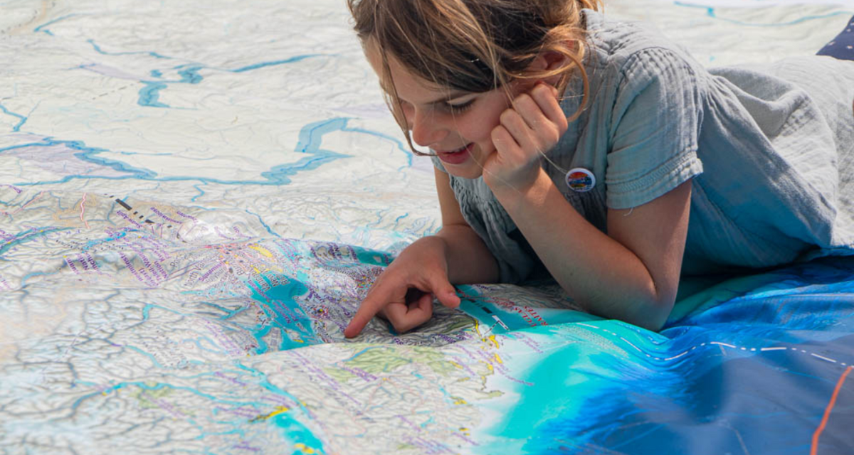 Smiling girl lying on a giant map on the ground. She is pointing to a feature on the map.